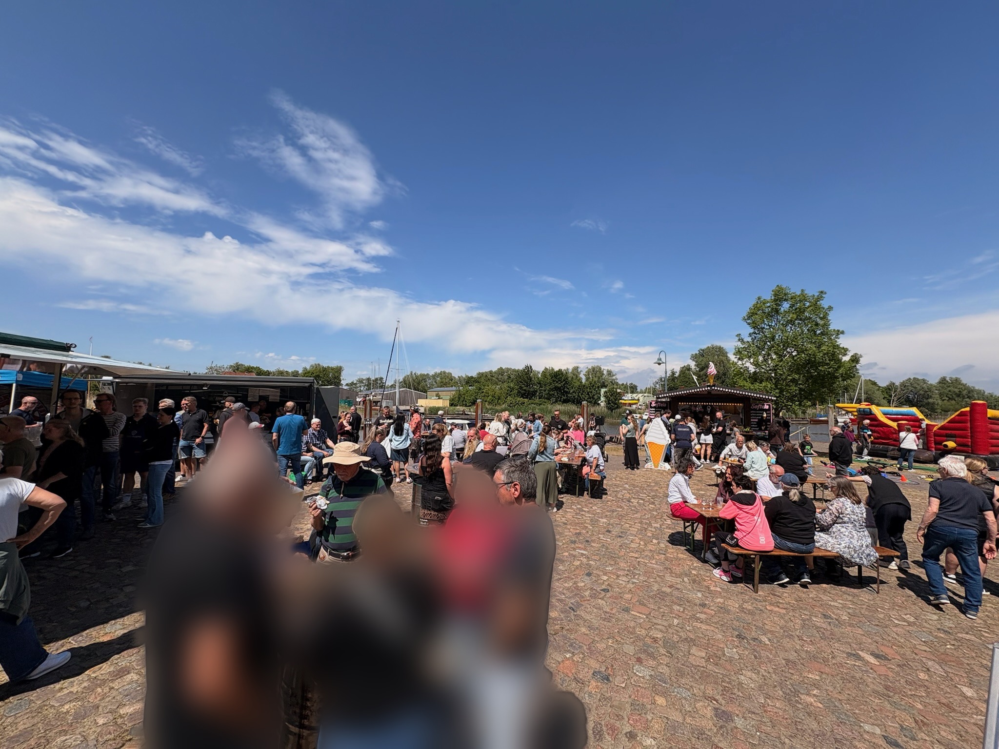 Hafenfest mit Menschenmenge, Imbissstand und Hüpfburg (Personen anonymisiert)
