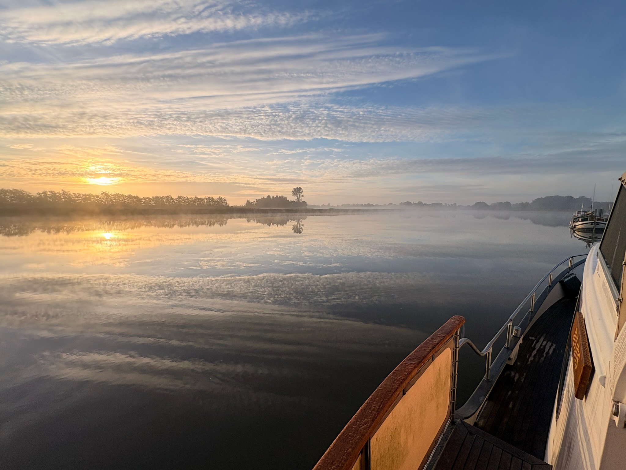 Sonnenaugang über der spiegelglatten Oste mit Nebel, von der Reling eines Bootes fotografiert